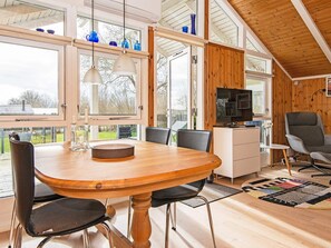 A modern interior with a wooden dining table, chairs, a television, and a view of the outdoors. - 4 Star Holiday Home in Juelsminde (Horsens)