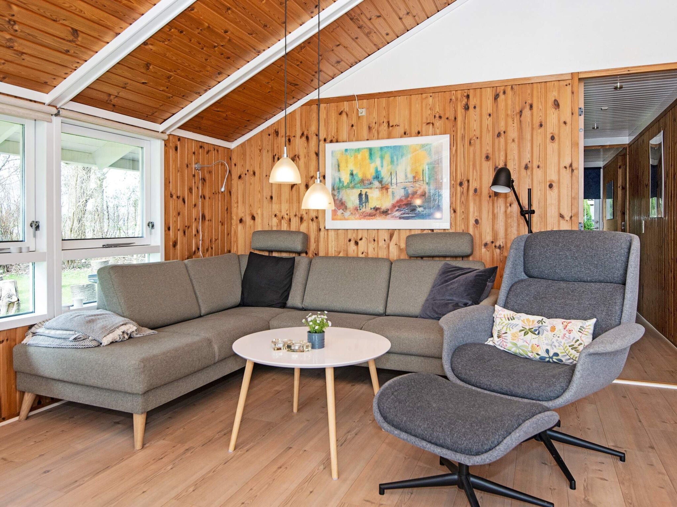 Un salon chaleureux avec un plafond en bois, un canapé gris, une table basse ronde et un fauteuil gris.