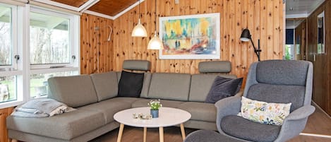 Un salon chaleureux avec un plafond en bois, un canapé gris, une table basse ronde et un fauteuil gris.
