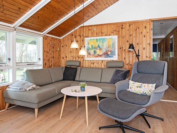 A cozy living room with a wooden ceiling, a grey sofa, a round coffee table, and a grey armchair. - 4 Star Holiday Home in Juelsminde (Horsens)