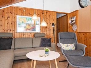 A modern living room with a wooden wall, a grey sofa, a grey armchair, a white coffee table, and pendant lights.
