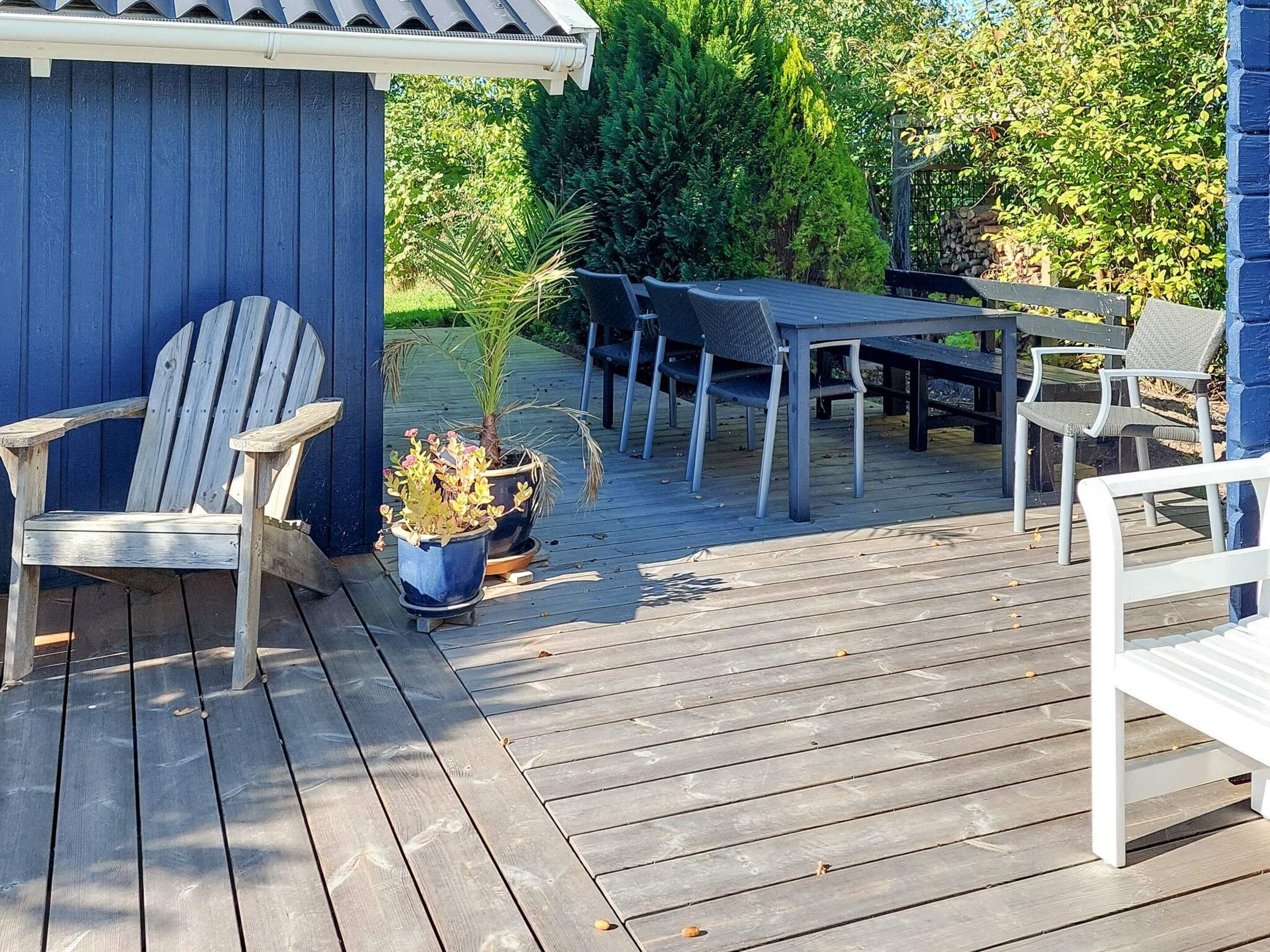 A wooden deck with a table and chairs, a potted plant, and a blue building.