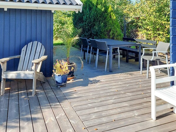 A wooden deck with a table and chairs, a potted plant, and a blue building.