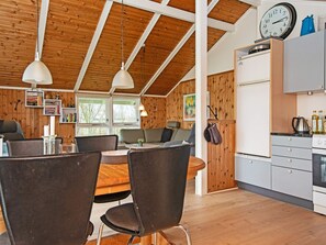 A modern kitchen with wooden beams, a dining area with a round table and chairs, and a view of the outdoors through large windows.
