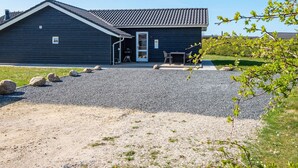 Een donkerblauwe woning met een pannendak, een grindpad en een klein terras met een tafel en stoelen.
