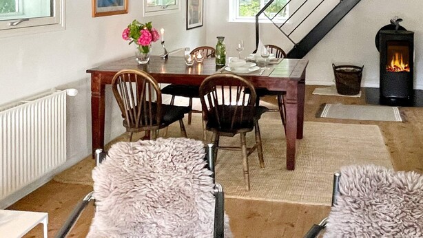 Comedor con una mesa preparada para cuatro personas, rodeada de sillas, una chimenea y un radiador.