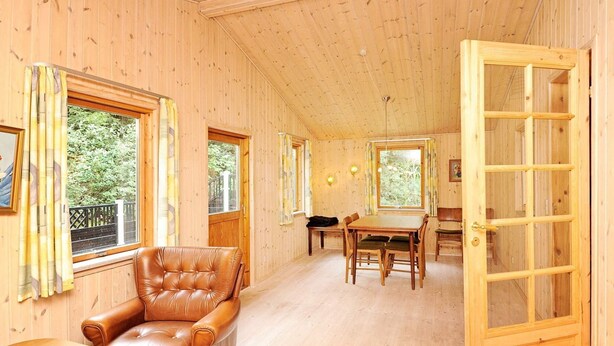 A wooden cabin interior with a dining area, a leather armchair, and a large window. - 4 Person Holiday Home in Ansager (Ansager)