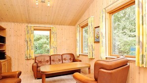 A cozy cabin interior with a wooden ceiling, a sofa, a dining table, and large windows with curtains. - 4 Person Holiday Home in Ansager (Ansager)
