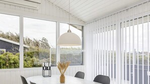 A dining area with a round table, chairs, a hanging light fixture, and a view of greenery outside. - 6 Person Holiday Home in Lokken (Lokken)