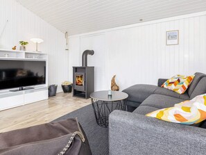 Ein modernes Wohnzimmer mit Flachbildfernseher, einer Couch, einem kleinen runden Tisch und einem Kaminofen.