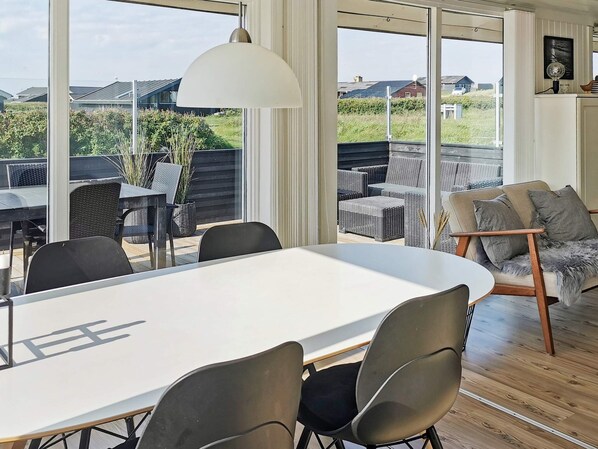 A modern interior with a large dining table, chairs, a sofa, and a large window offering a view of the outdoors.