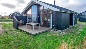 Ein modernes Haus mit einem großen Panoramafenster, einer Holzterrasse und einem Grill.
