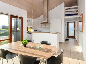 A modern kitchen with a central island, a dining area with a table and chairs, and a view through a glass door.