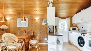 Una cocina moderna con electrodomésticos blancos, un comedor con sillas de mimbre y paredes de madera.