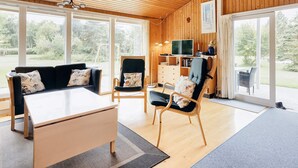 Un salón amplio con techo de madera, ventanas grandes, un sofá, una silla, un televisor y una estantería.