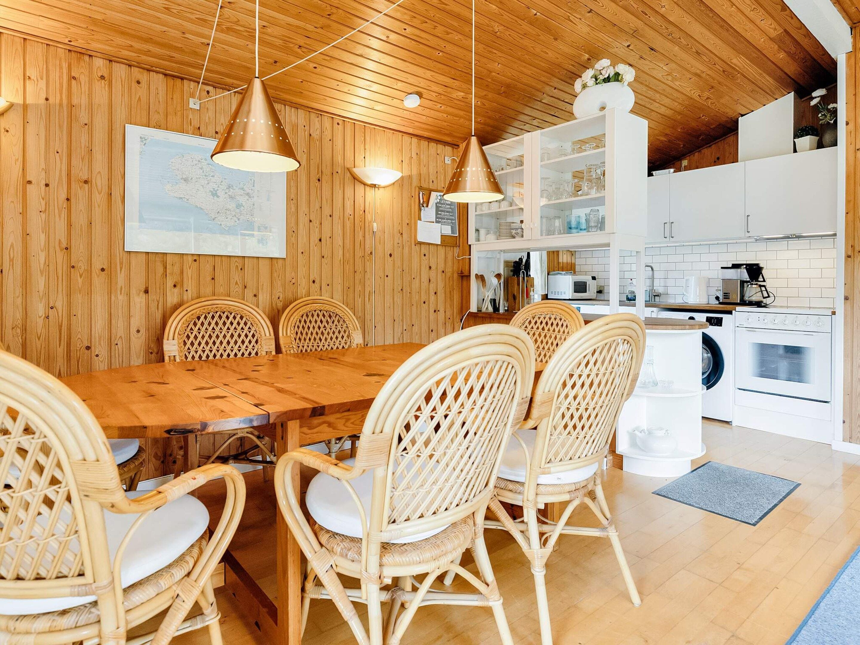 A wooden-paneled room with a dining table and chairs, a kitchen area with appliances, and a hanging light fixture.