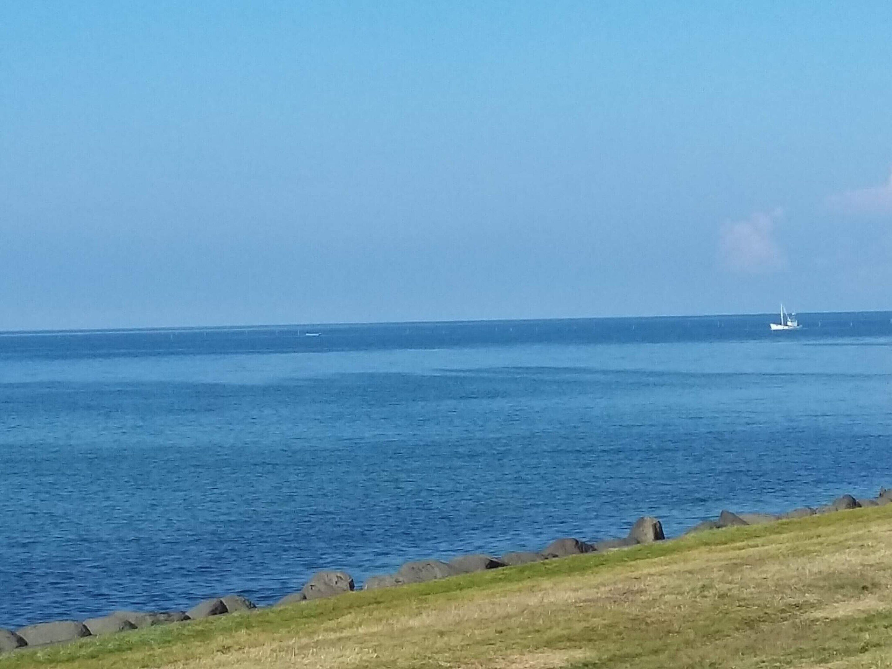 Blick auf die Küste mit einem Wasserlauf, einer grasbewachsen Fläche und einer felsigen Uferlinie.