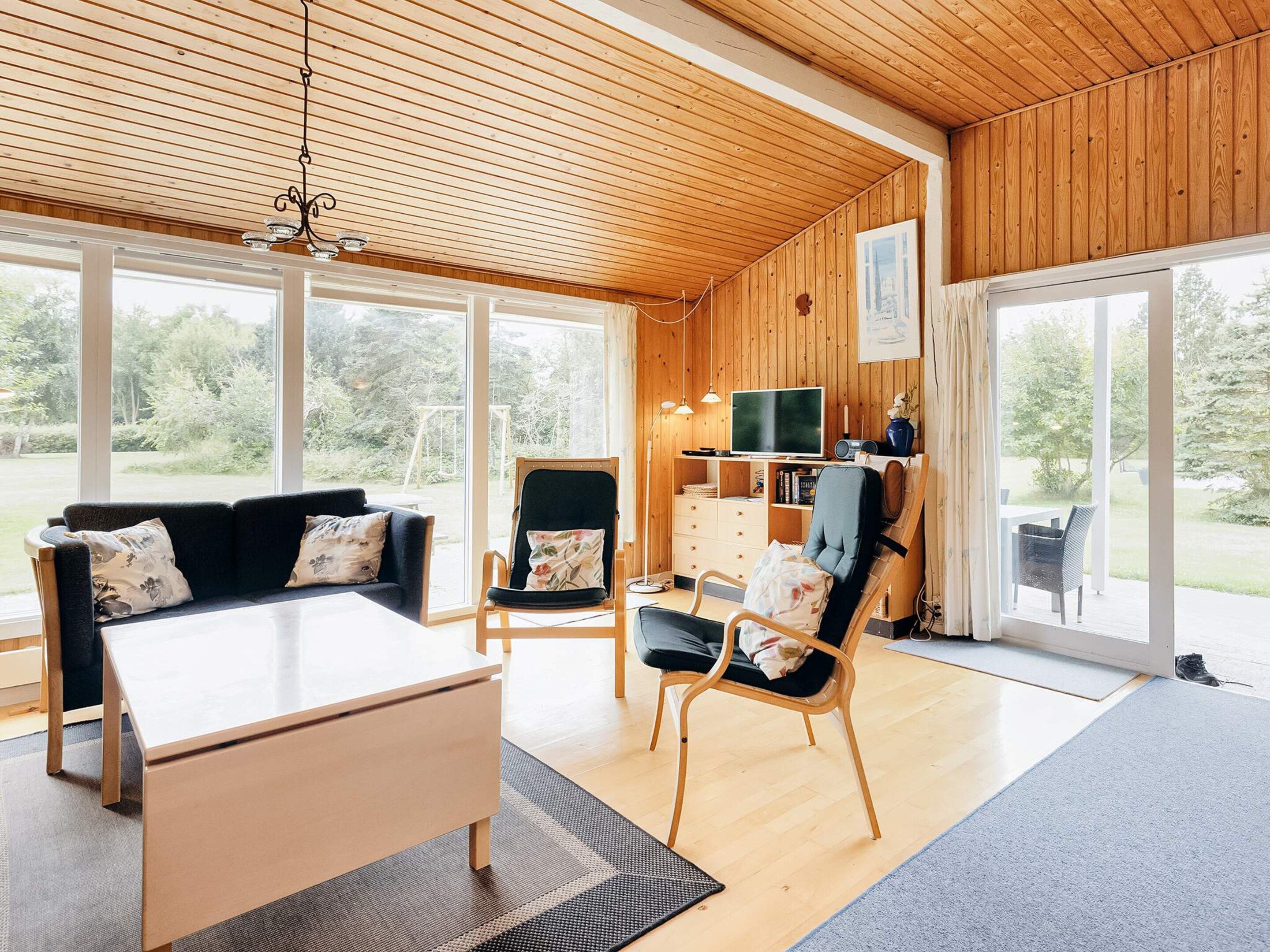 A spacious living area with a sofa, chairs, a TV, and a wooden ceiling.