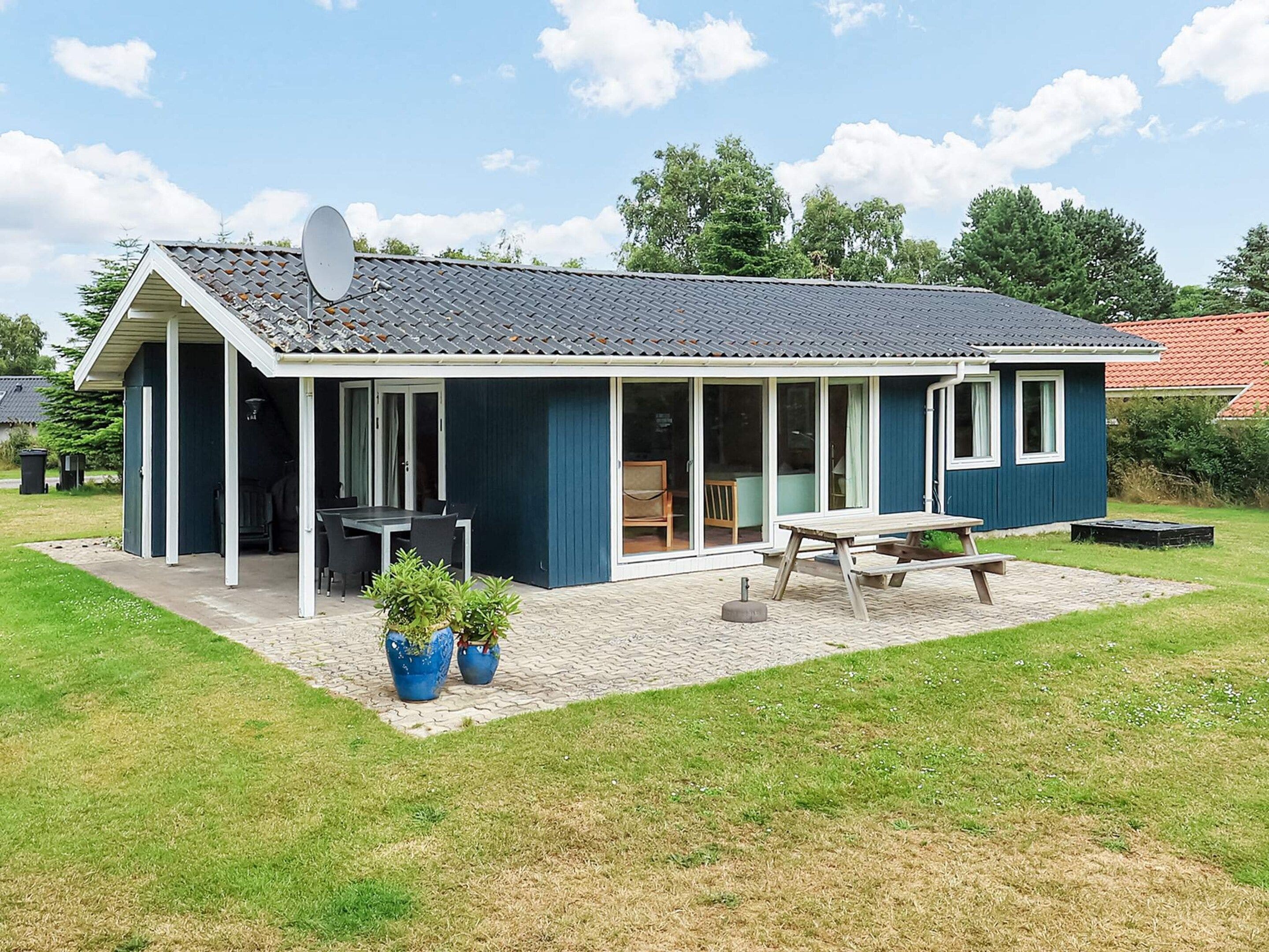 A single-story house with a covered patio, a dining table, and two potted plants.