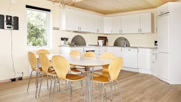 A modern kitchen with white cabinets, a wooden dining table with chairs, and a large window. - 8 Person Holiday Home in Vestervig-by Traum (Vestervig)