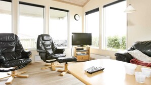 A living room with a wooden table, two black leather chairs, a television on a wooden stand, and a view of the outdoors through large windows. - 8 Person Holiday Home in Vestervig-by Traum (Vestervig)