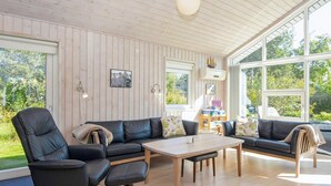 A modern living room with a wooden ceiling, large windows, a black leather sofa, a wooden coffee table, and a black armchair. - Serene Holiday Home in Juelsminde near Beach (Juelsminde)