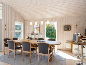 A dining area with a wooden table and chairs, pendant lights, and a view of greenery outside. - Serene Holiday Home in Juelsminde near Beach (Juelsminde)
