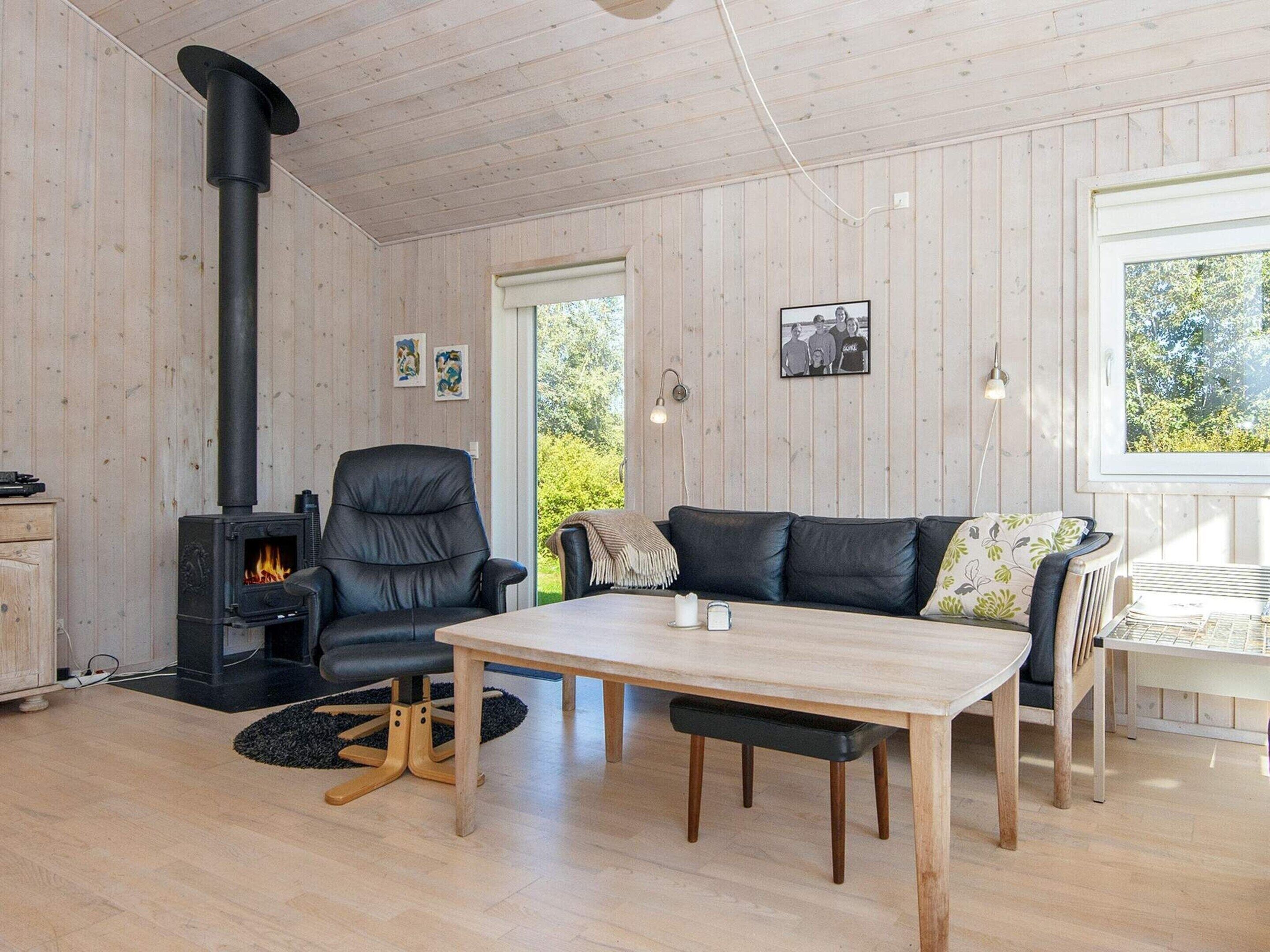 Ein gemütlicher Raum mit Holzeinrichtung, einem schwarzen Ledersessel, einem Holztisch und einem schwarzen Kaminofen.