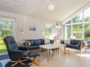 A modern living room with a wooden ceiling, large windows, a black leather sofa, a wooden coffee table, and a black armchair. - Serene Holiday Home in Juelsminde near Beach (Juelsminde)
