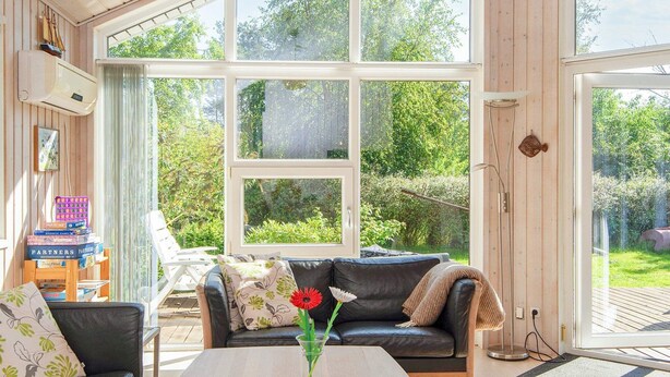 A cozy living room with a black leather sofa, a coffee table, and a large window offering a view of the garden. - Serene Holiday Home in Juelsminde near Beach (Juelsminde)