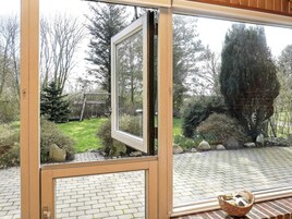 A room with a large window, a brick floor, and a view of a garden with trees and a swing set.