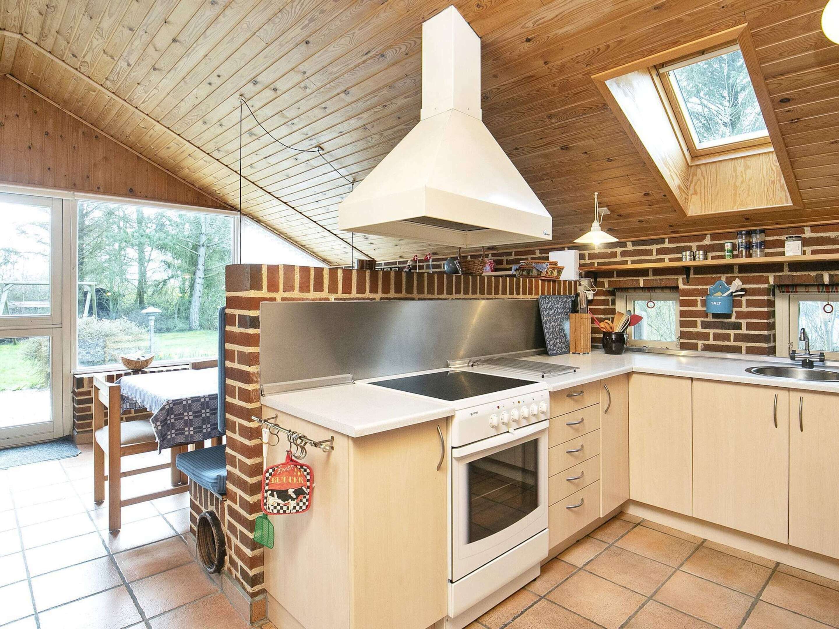 A kitchen with a brick accent wall, a large island with a stove, and a window overlooking a garden.