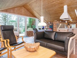 A modern living area with a wooden ceiling, a black leather sofa, a wooden coffee table, and a wicker side table.