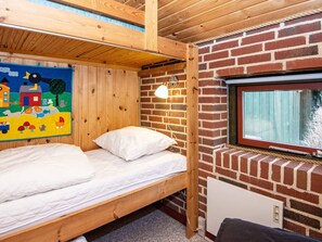 A single wooden bunk bed with a white mattress and pillow, a brick wall, and a window with a view of the outside. - Rustic Holiday Home in Jutland near Sea (Ulfborg)