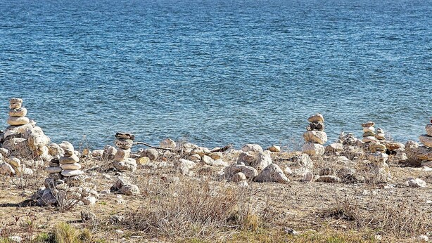 A coastal landscape with a clear view of the sea and a rocky shoreline with stacks of stones.
