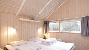 A wooden-paneled room with a bed, a window, and a wall-mounted light fixture.