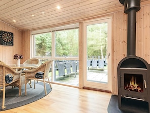 A cozy room with a fireplace, wicker furniture, and large windows offering a view of the outdoors. - 4 Star Holiday Home in Oster Assels (Øster Assels)