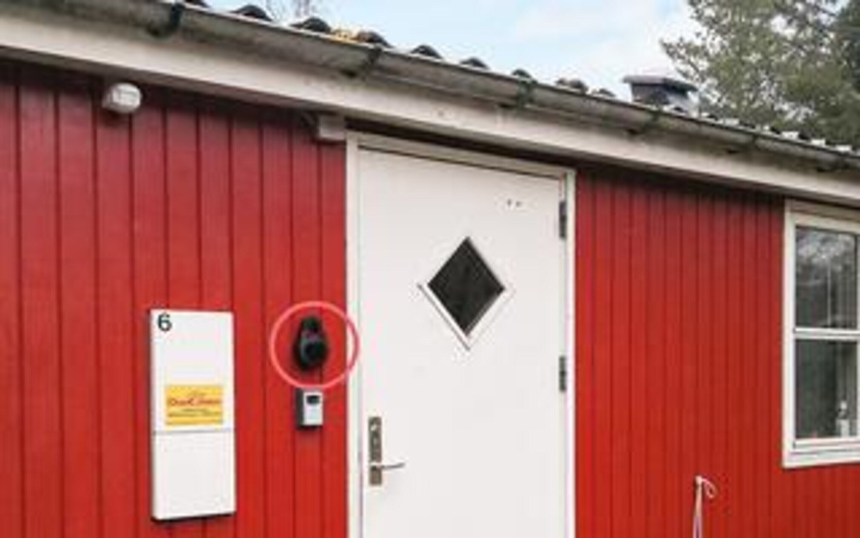 A red building with a white door, a number 6 sign, and a security camera.