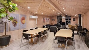 Een kamer met houten wanden en plafond, een grote kamerplant, een lange tafel met stoelen, een bank en een televisie.