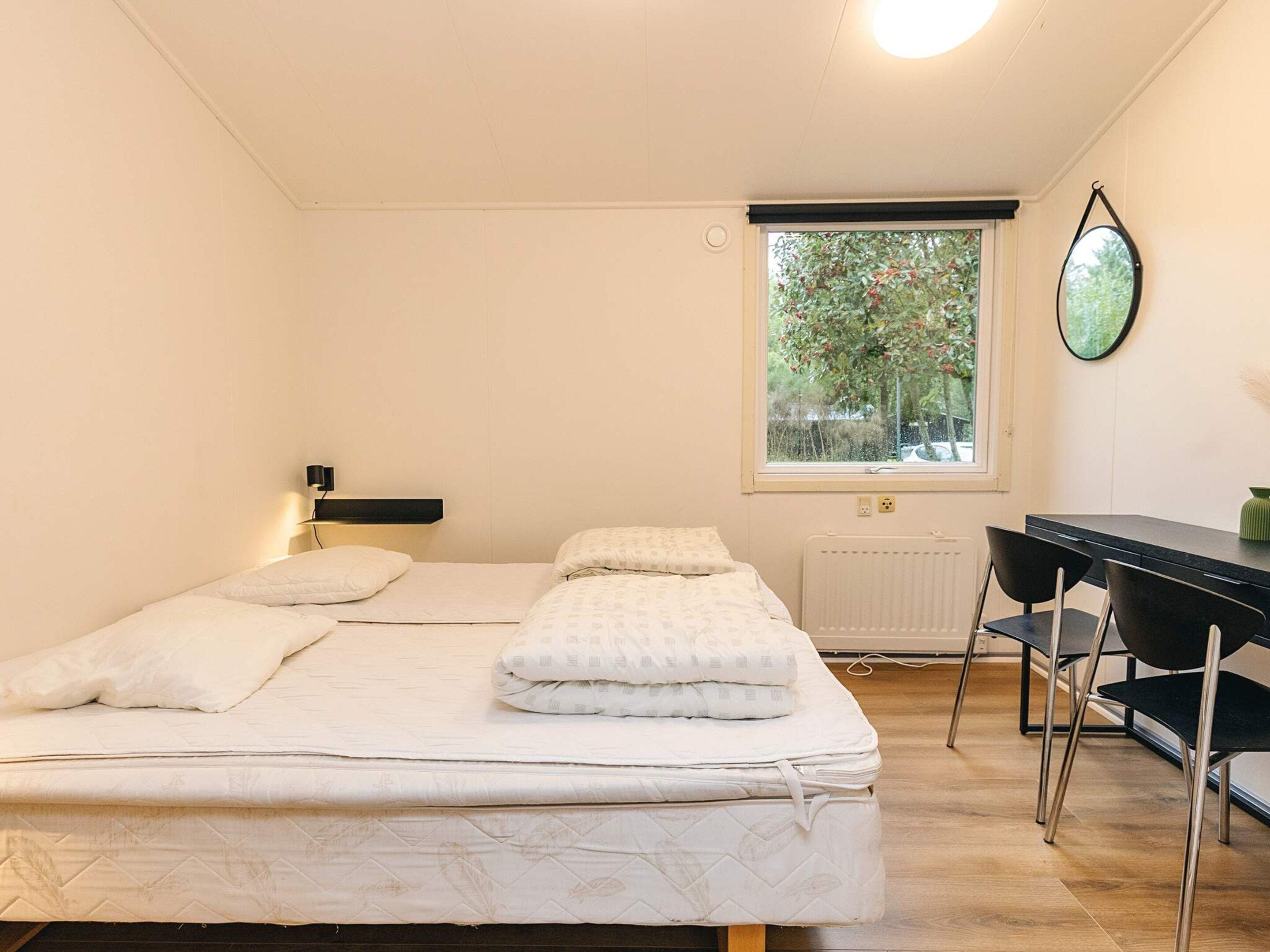 A room with two beds, a desk, and a window with a view of trees.