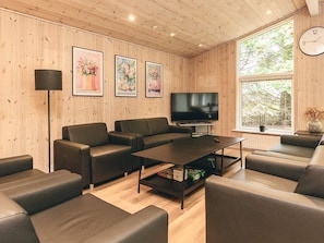 A modern living room with a flat-screen TV, leather sofas, a coffee table, and framed floral artwork on the wall. - 4 Star Holiday Home in Oster Assels (Øster Assels)