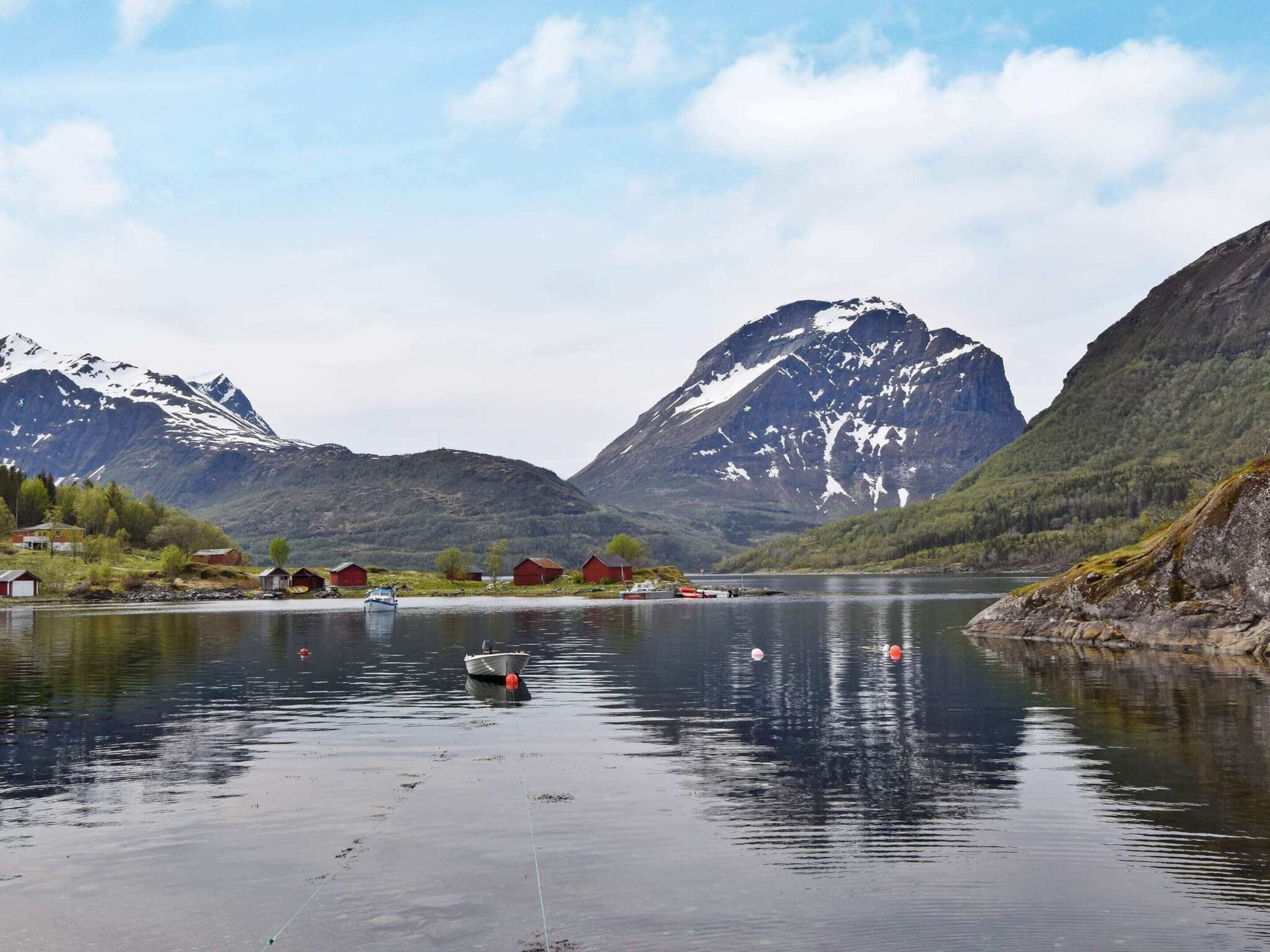 En stilla sjö med båtar, röda hus och berg i bakgrunden.