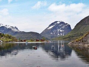 Ein ruhiger See mit Booten, roten Häusern und Bergen im Hintergrund.