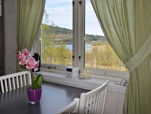 A room with a view of a lake and hills, a purple orchid on a table, a white chair, and a window with a curtain. - Holiday Home in Inndyr (Gildeskal)