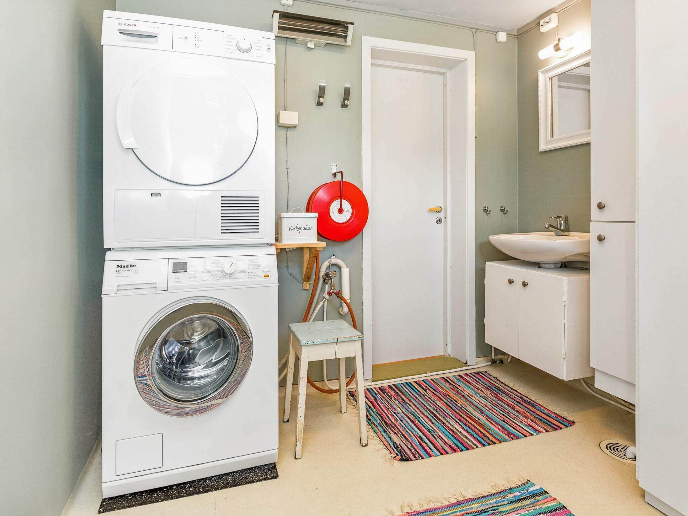 A compact laundry room with a front-loading washer and dryer, a small sink, and a mirror.