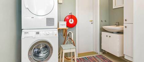 A compact laundry room with a front-loading washer and dryer, a small sink, and a mirror.