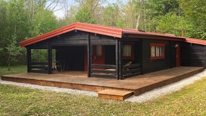 A cabin with a red roof, wooden deck, and a covered porch area.
