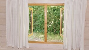 A window with white curtains, wooden frame, and a view of greenery outside.