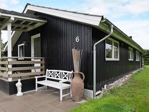 A black building with a white porch, a bench, and a large vase.