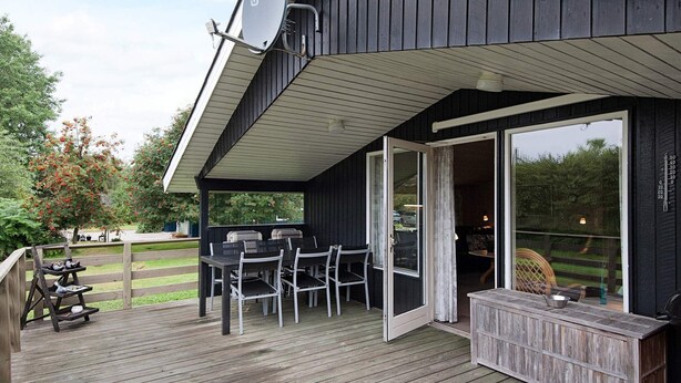 A covered outdoor area with a table and chairs, a barbecue grill, and a wooden deck.